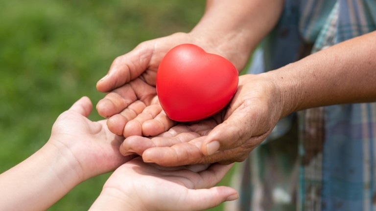 The red rubber heart on hands of elderly and child. Showed the cooperate, love, care, charity of people with differences diversity for sustain develop of farmer, community, society and the environment csr