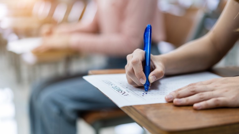 Close up of young female university students concentrate on doing examination in the classroom. Girl student writes the answer of the examinations on answer sheet in the classroom.